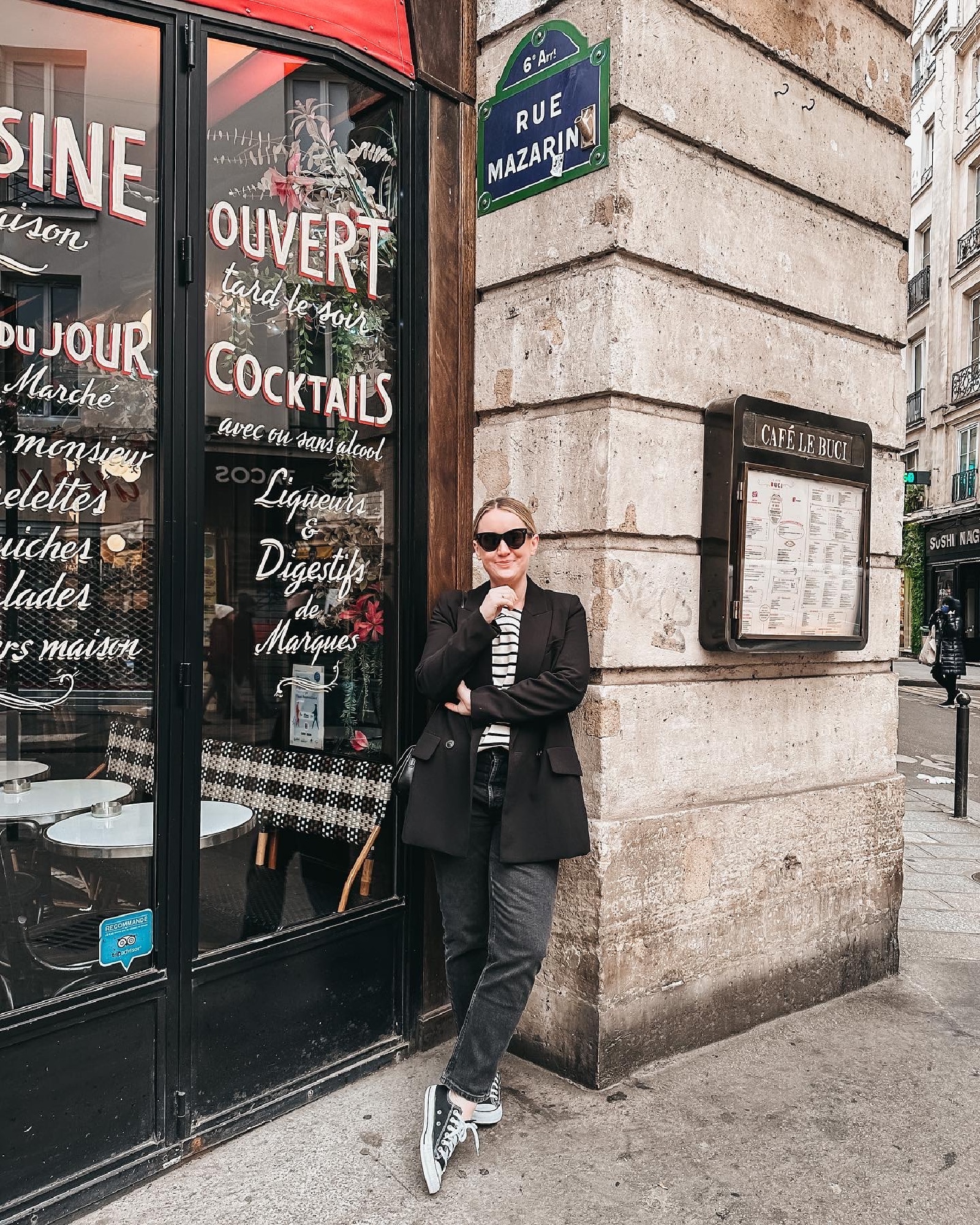 Fall Outfit Ideas with Jeans Whit Whimsy wearing jeans with a black blazer and converse leaning against a restaurant outdoor wall