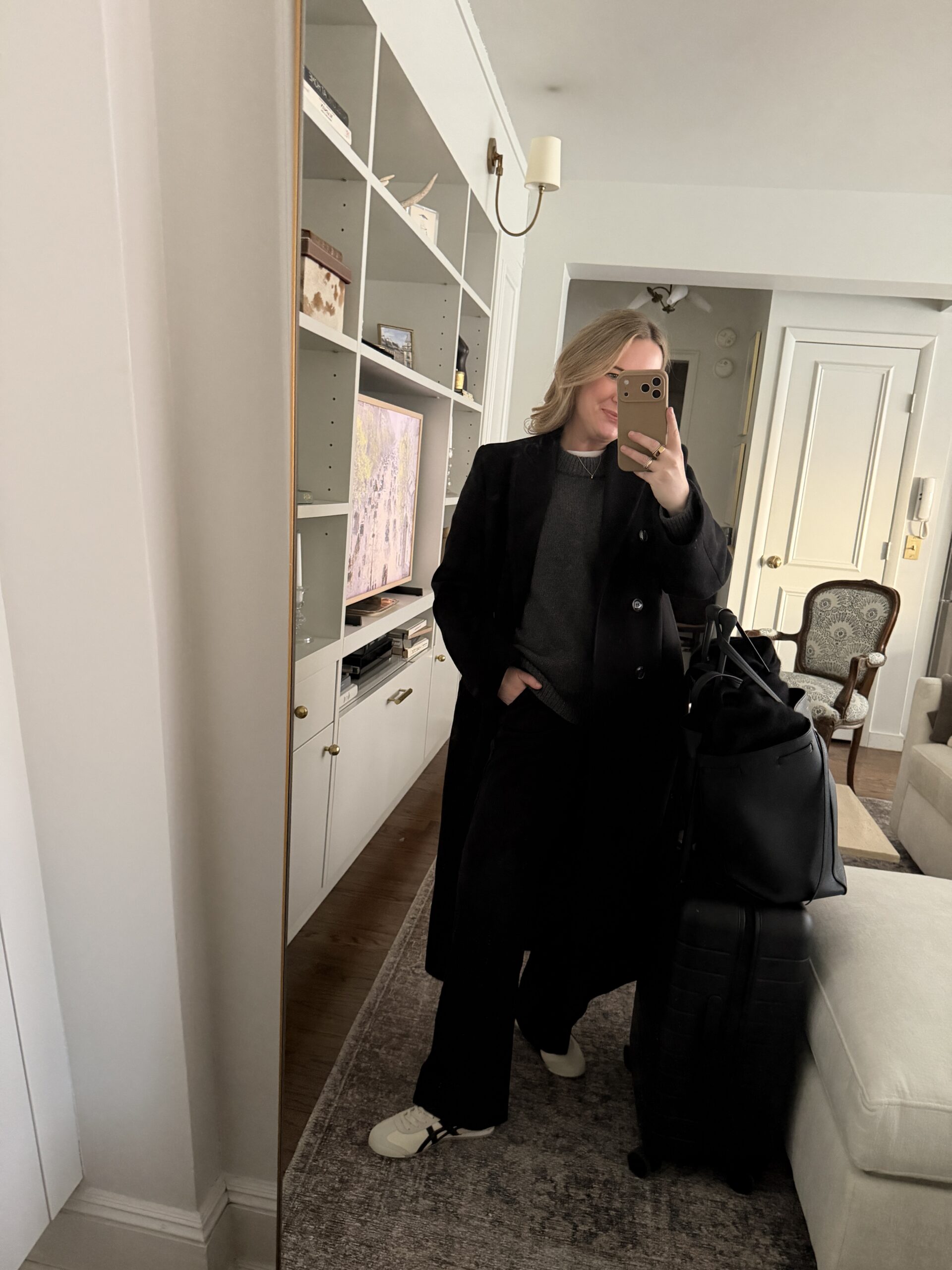 Easy Travel Outfits wit & whimsy wearing black travel outfit with wool coat, knit sweater and wide leg trousers