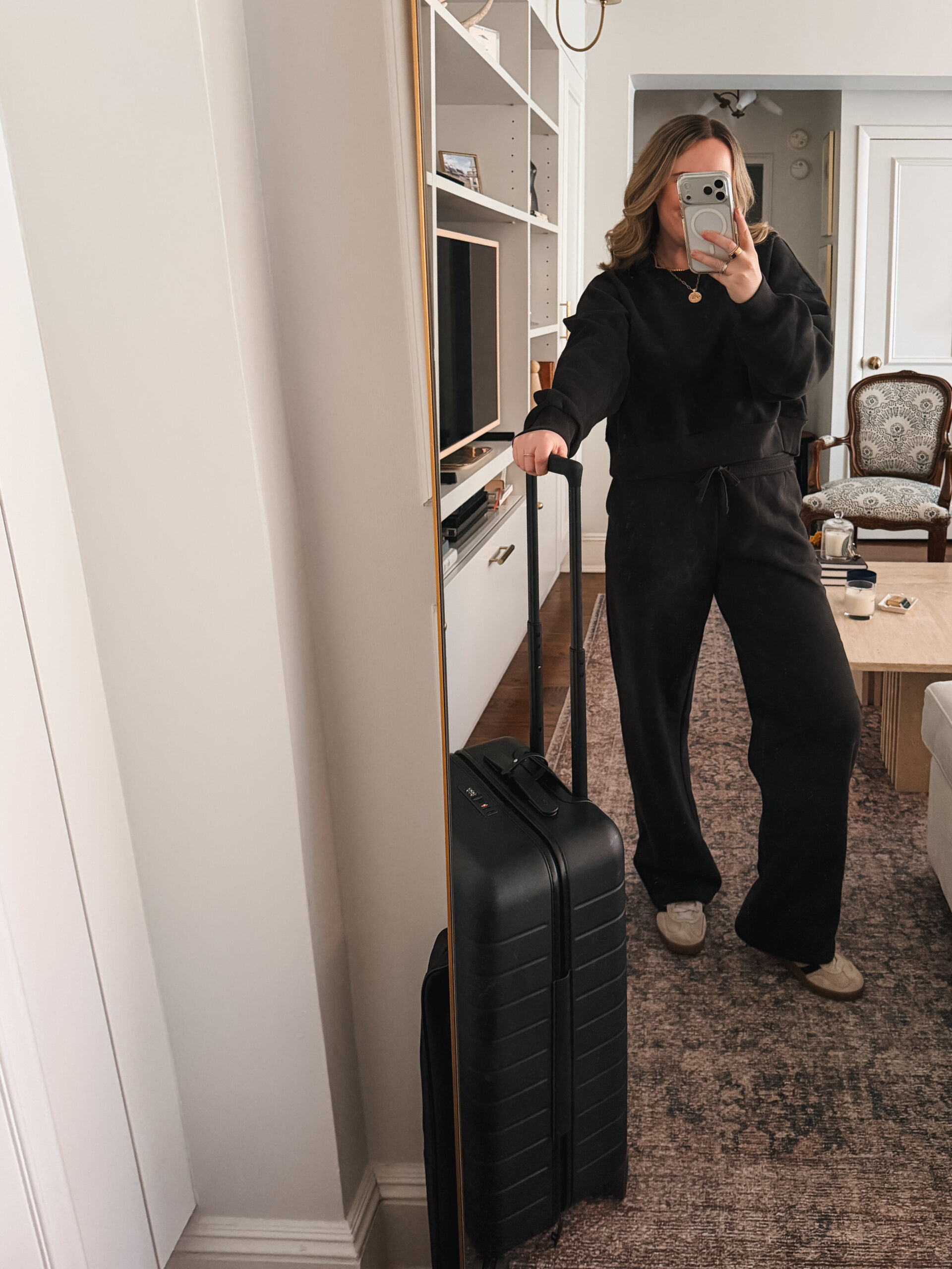 Easy Travel Outfits All black matching travel set with sweatshirt and wide leg sweatpants styled with carry-on suitcase