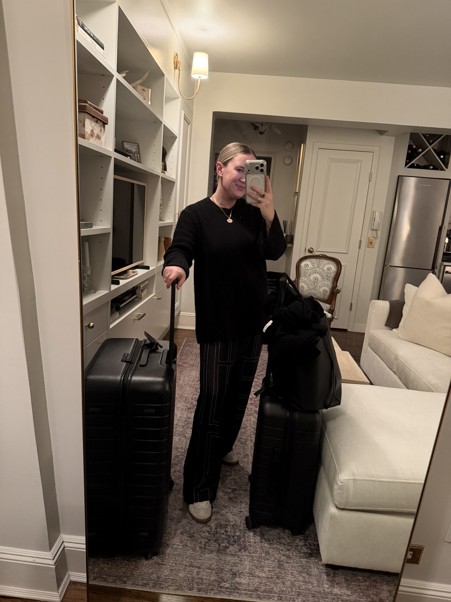 Easy Travel Outfits wit & whimsy wearing a black sweater and wide leg trousers styled with carry-on luggage