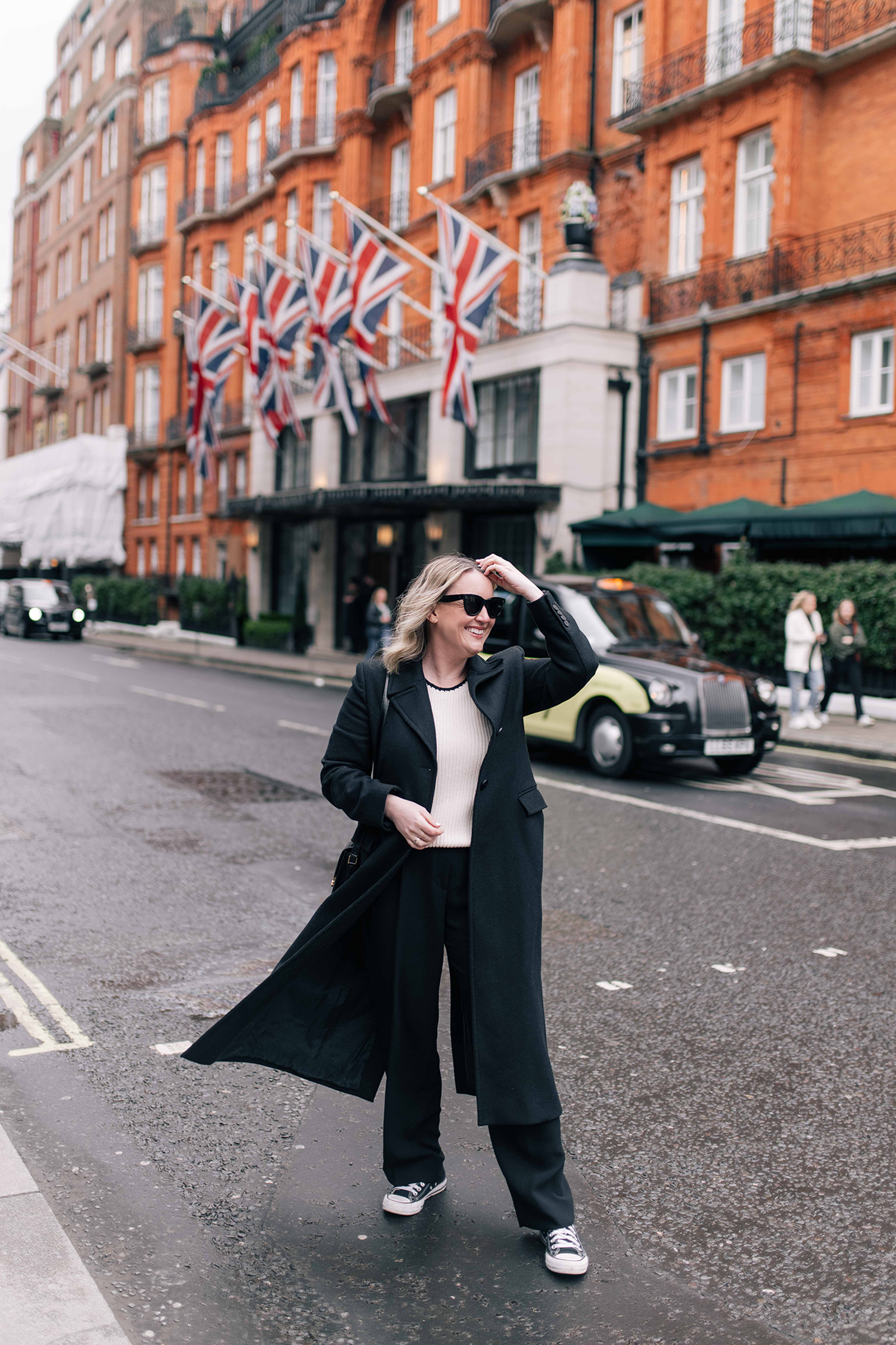 What Shoes to Wear in London Meghan Donovan of wit & whimsy showcasing a chic winter ensemble featuring a tailored coat, scarf, and boots in front of a London backdrop.