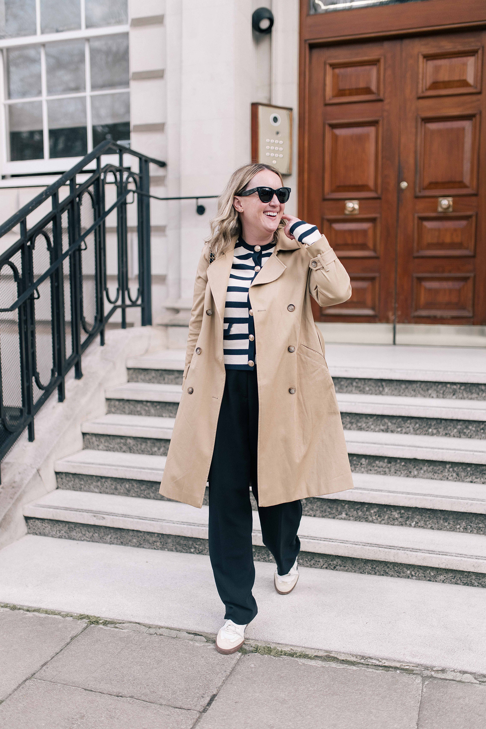 What to Pack for the Cotswolds: beige trench coat, navy striped sweater, wide-leg trousers, and white sneakers